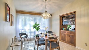 A dining area with a wooden table, chairs, and a chandelier. There is a cabinet with dishes and a plant. - Retro St Pete Home w/ Private Heated Pool (St. Petersburg)
