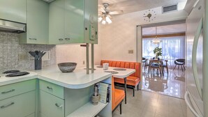 A kitchen with green cabinets, a white countertop, and a dining area with an orange booth. - Retro St Pete Home w/ Private Heated Pool (St. Petersburg)