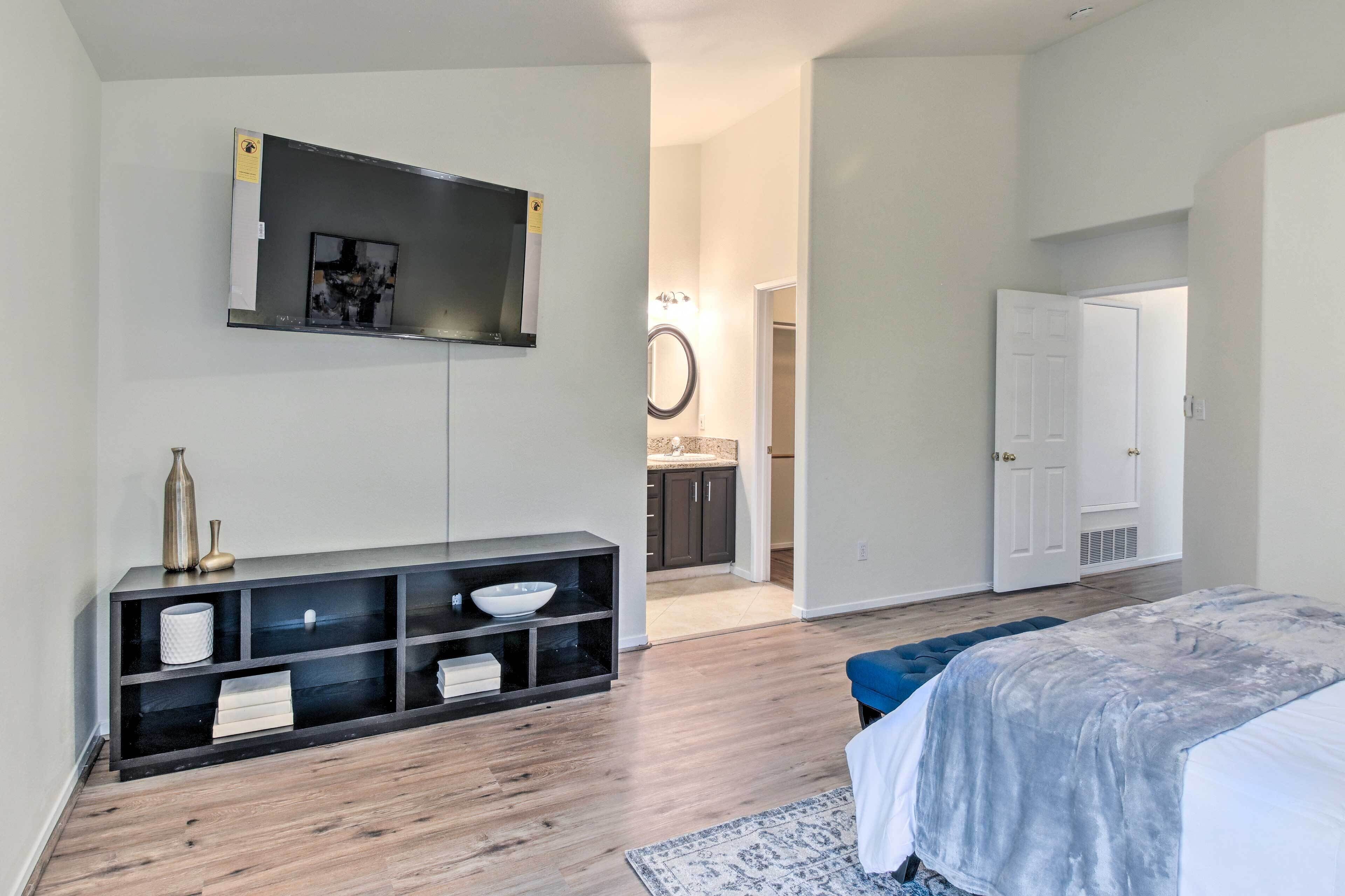 Een slaapkamer met een bed, een aan de muur bevestigde televisie, een console met decoratieve objecten en een hal die naar een badkamer leidt.