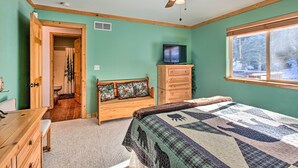 Une chambre à coucher comprenant un lit, une commode en bois, un téléviseur, une fenêtre donnant sur des arbres et un ventilateur de plafond.