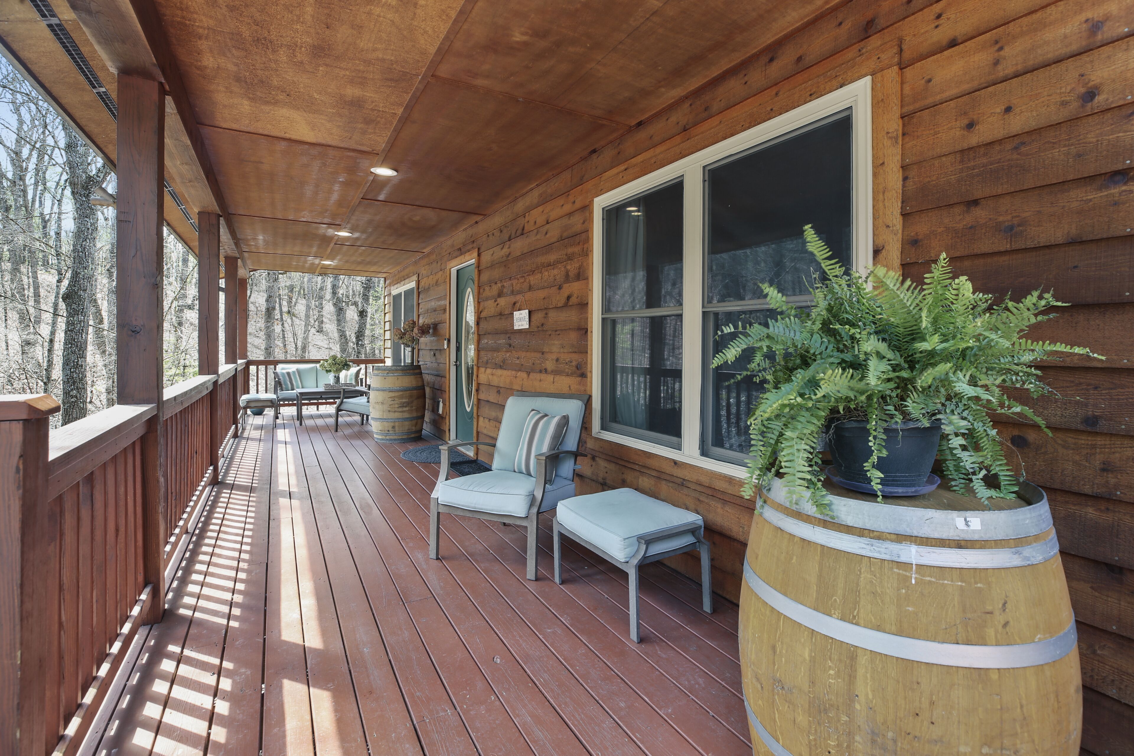 A wooden deck with a covered area, seating, and a large window.