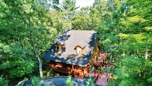 A cabin surrounded by dense forest with a wooden deck and a covered porch. - Acorn Ridge: Modern Shenandoah Mountain 4 Bedroom 4 Bathroom, Firepit, Theater (Basye)