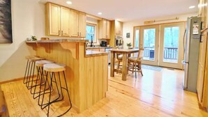 A spacious kitchen with wooden cabinets, a central island with stools, and a dining area with a table and chairs. - Acorn Ridge: Modern Shenandoah Mountain 4 Bedroom 4 Bathroom, Firepit, Theater (Basye)