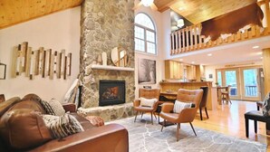 A spacious living area with a stone fireplace, leather furniture, and a high ceiling with wooden beams. - Acorn Ridge: Modern Shenandoah Mountain 4 Bedroom 4 Bathroom, Firepit, Theater (Basye)