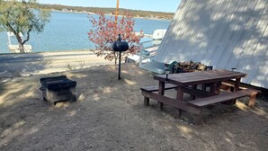 A picnic table and grill area with a view of a lake and boats in the background. - Modern Relaxing Lakeside Cabin #3 (Cisco)
