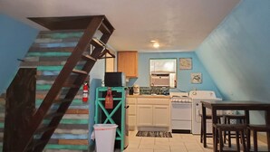A compact kitchen with a wooden staircase, a small dining area, and a trash bin. - Modern Relaxing Lakeside Cabin #3 (Cisco)