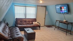 A living room with a brown leather sofa, a matching armchair, a small ottoman, and a television mounted on the wall. - Modern Relaxing Lakeside Cabin #3 (Cisco)