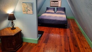 A bedroom with a sloped ceiling, a bed with a blue and white bedspread, a bedside lamp, a small table, and a painting on the wall. - Modern Relaxing Lakeside Cabin #3 (Cisco)