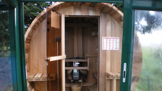Een houten sauna met een deur, een metalen bak en een bord aan de muur.