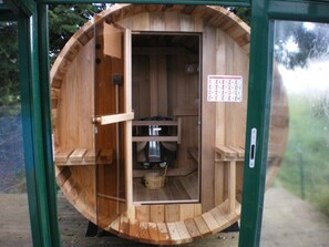 Una sauna de madera con puerta, un recipiente metálico y un cartel en la pared.