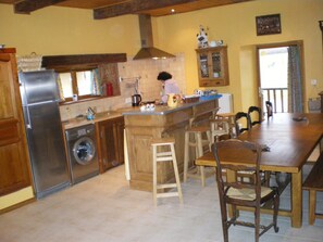 A kitchen with a large island, wooden cabinets, a stainless steel refrigerator, and a washing machine.
