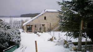 Een stenen gebouw met een schuin dak, omgeven door besneeuwde grond en bomen.