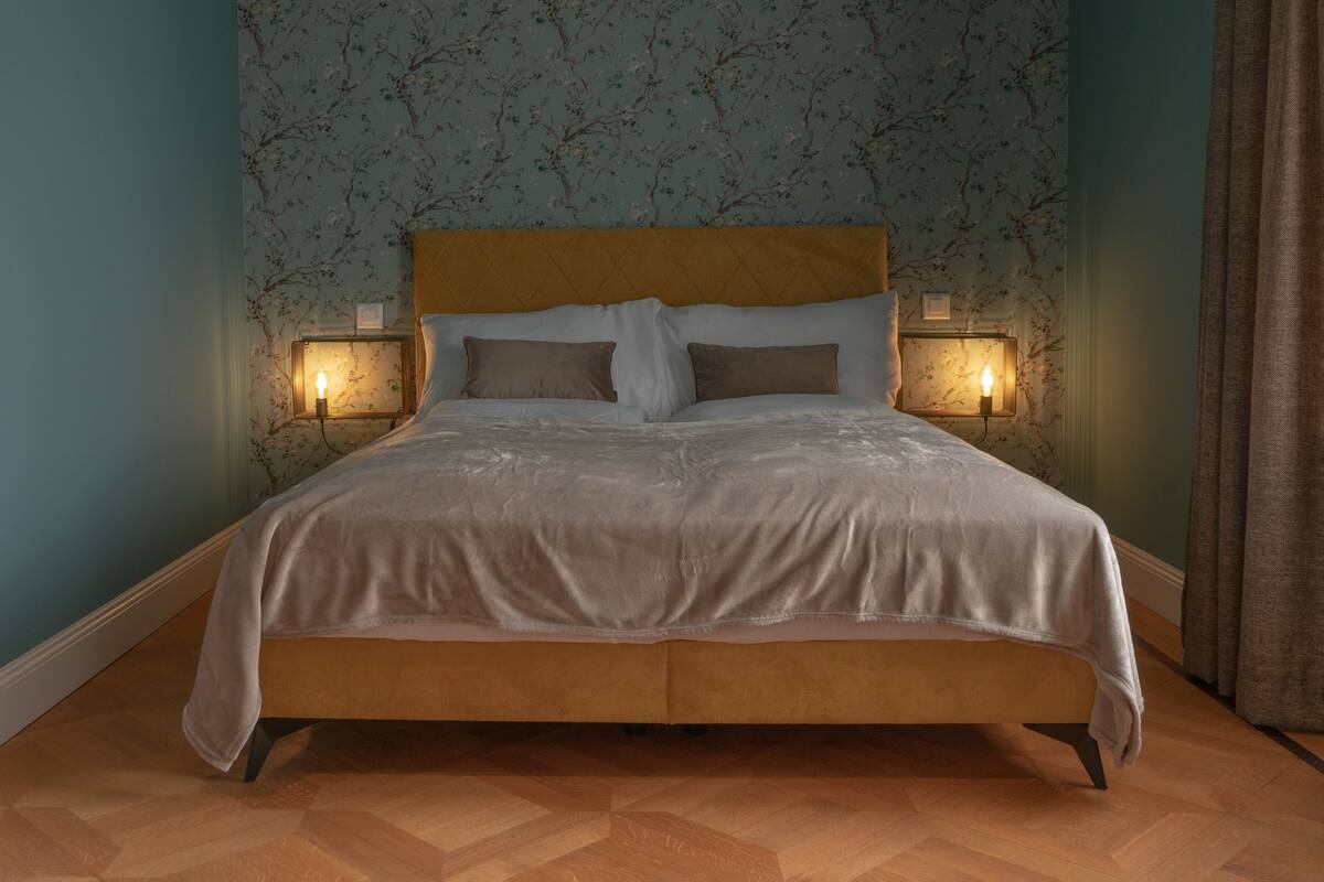 A bed with a wooden headboard, two bedside lamps, and a floral wallpaper pattern.