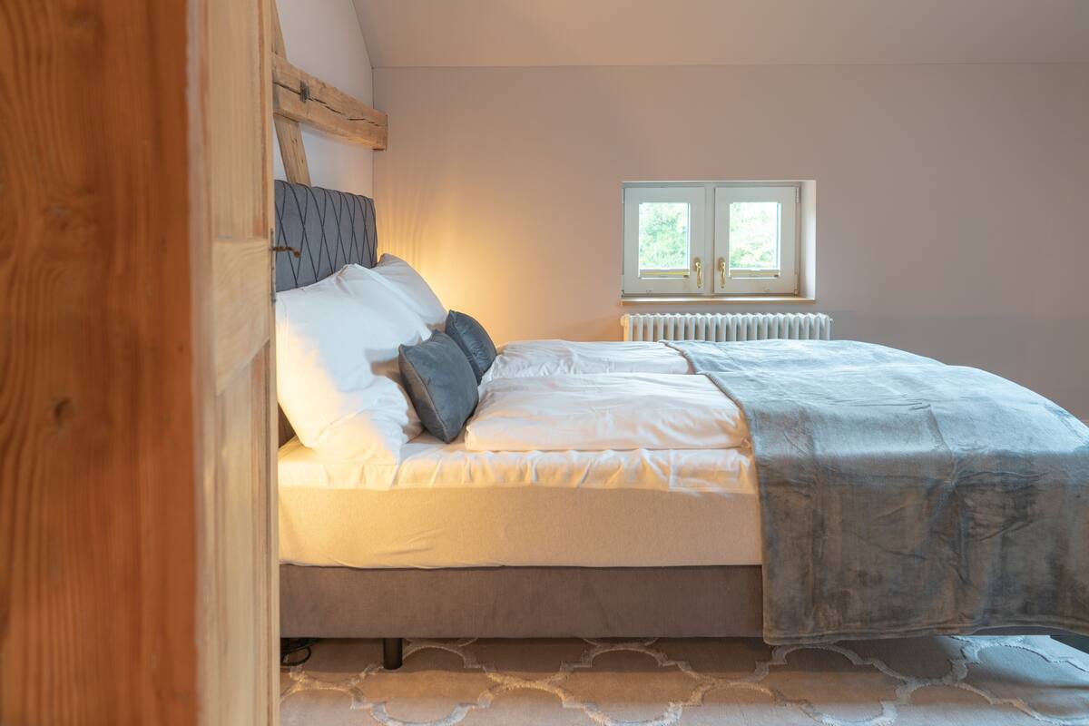 A bedroom with a bed, pillows, a window, and a radiator.