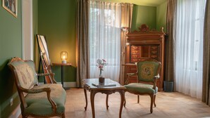 Et værelse med to grønne polstrede stole, et træbord med en vase blomster, et spejl og et træskab med skuffer.