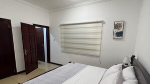A bedroom with a bed, a window with blinds, a door, and a ceiling light. - Quiet escape, good security and serene environment (Accra)