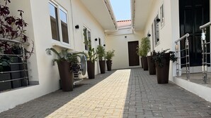 A paved walkway with potted plants on either side, leading to a building entrance with a black door. - Quiet escape, good security and serene environment (Accra)