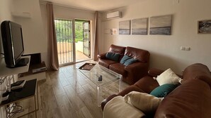 A living room with a brown leather sofa, a glass coffee table, a TV, and a sliding glass door leading to an outdoor area. - NEW LAUNCH!!! Wyndham Beach and Pools Resort in La Cala, Mijas & Fuengirola (Las Lagunas de Mijas)
