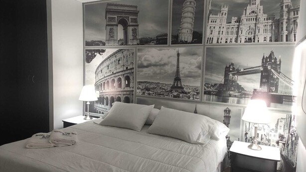 Ein Hotelzimmer mit einem großen Bett, zwei Nachttischen mit Lampen und einer Wand, die mit Schwarz-Weiß-Fotos berühmter Wahrzeichen geschmückt ist.