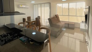 Eine moderne Küche mit Gasherd, einem Esstisch mit Stühlen, einer Couch und einem Fernseher in einem Wohnbereich mit großen Fenstern.