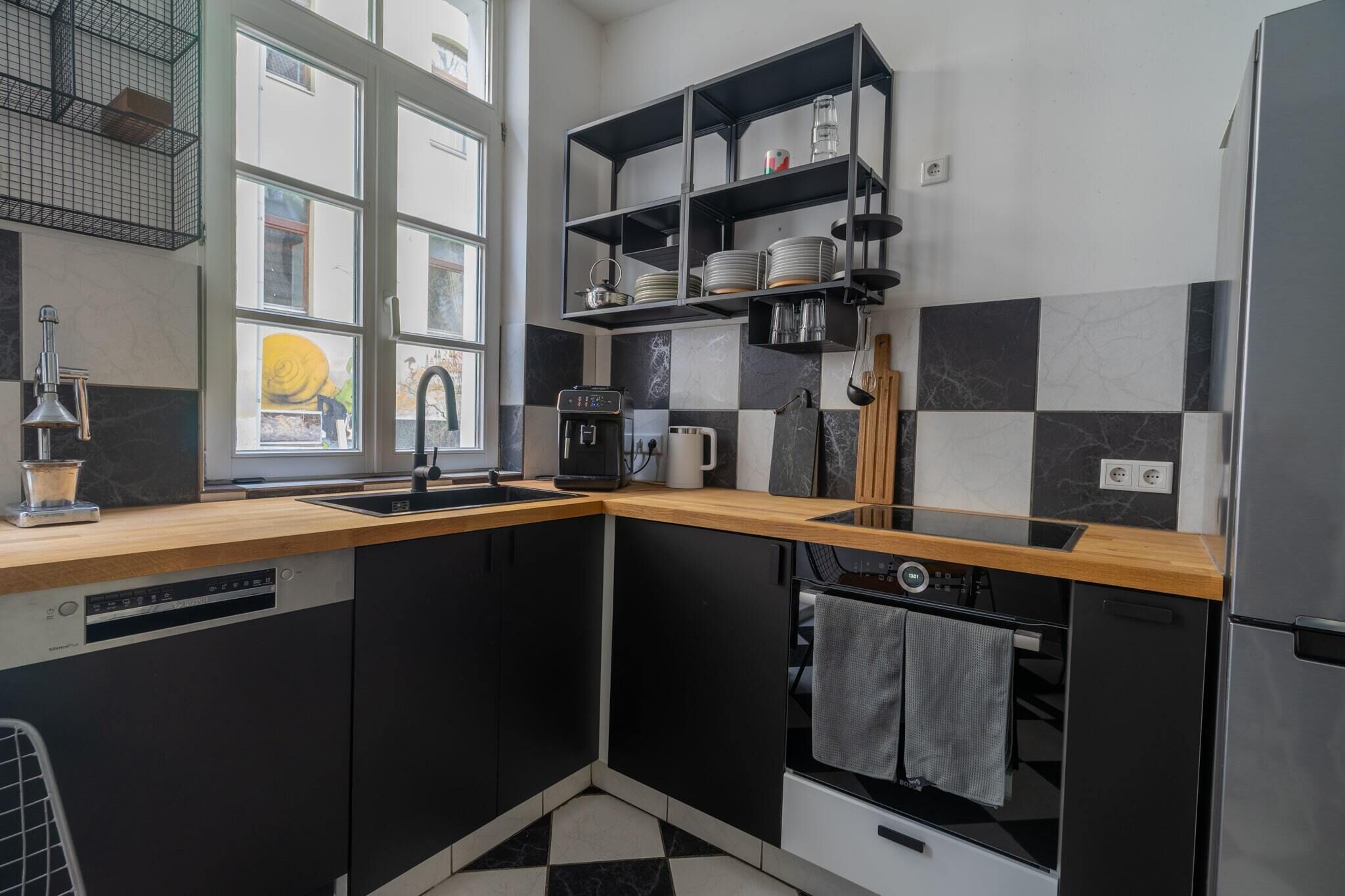 Une cuisine moderne avec des meubles de couleur noire, un plan de travail en bois, un lave-vaisselle encastré, une machine à café et un réfrigérateur.