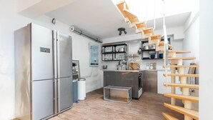 Una cucina compatta con frigorifero integrato, un piccolo lavandino e mensole in legno sopra il piano di lavoro.