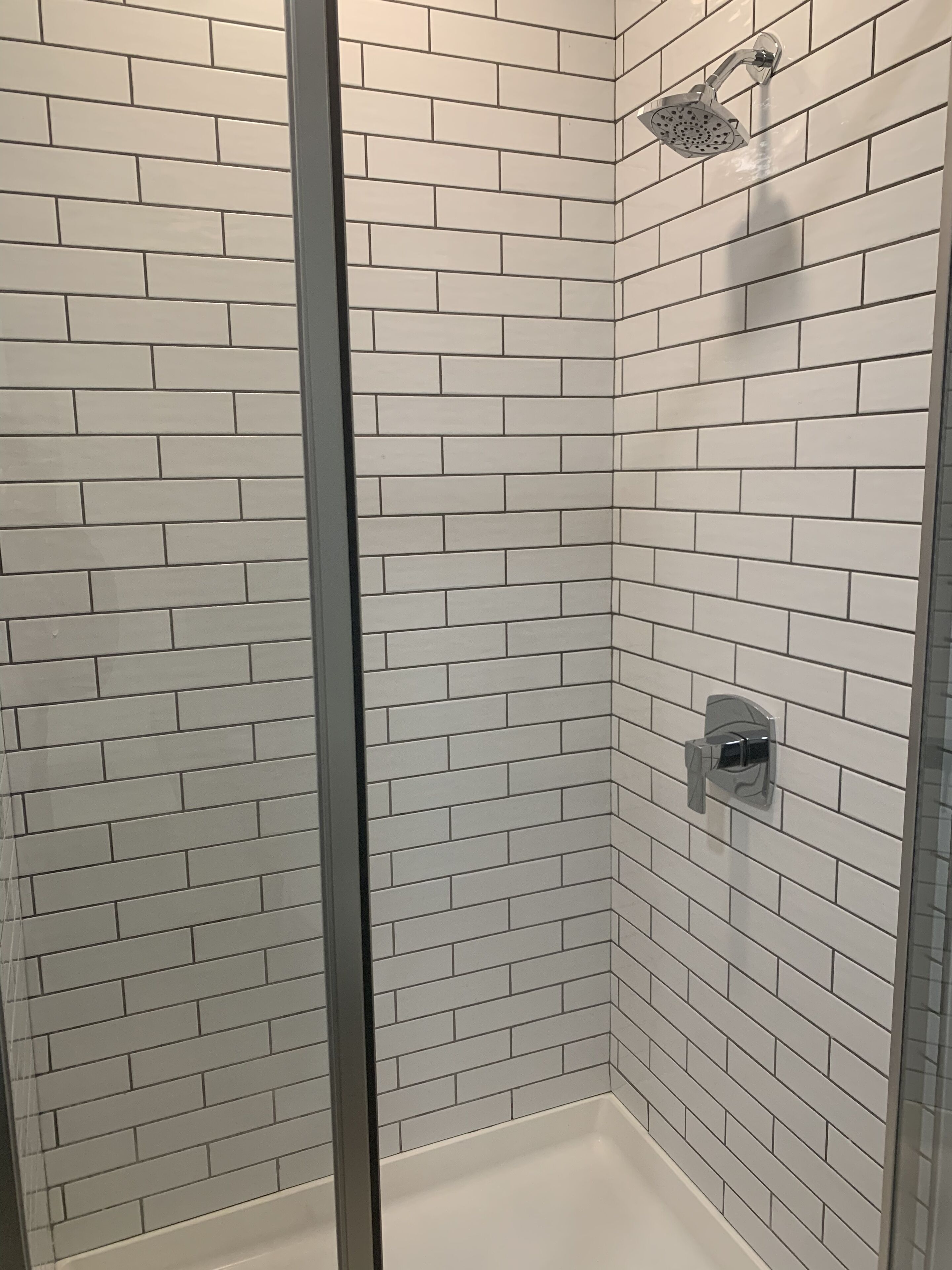 Ducha con azulejos blancos tipo metro y puerta de vidrio.