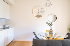 Une cuisine moderne avec des meubles blancs, un coin repas doté d’une table et de chaises en verre, et un miroir fixé au mur.