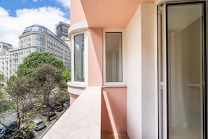 Un edificio moderno con fachada de vidrio curvo, un balcón estrecho con una puerta y un árbol en primer plano.