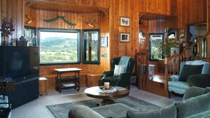 Un intérieur de chalet chaleureux avec des murs en bois, une grande fenêtre offrant une vue panoramique, une cheminée et un coin salon confortable.