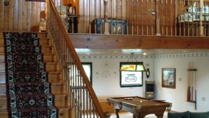 Un intérieur en bois avec un escalier, une table de billard et un canapé vert.
