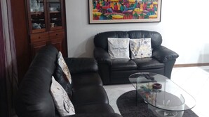 A living room with two black leather sofas, a glass coffee table, a cabinet with glass doors, and a colorful abstract painting on the wall. - One step away (Arezzo)