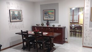 A dining area with a wooden table and chairs, a kitchen area with a refrigerator and cabinets, and a hallway leading to another room. - One step away (Arezzo)