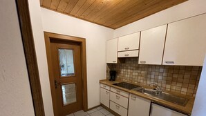 Eine kleine Küche mit weißen Schränken, einer Holzbalkendecke und Fliesenboden.