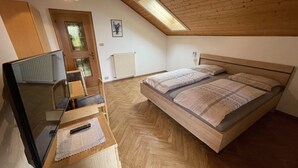 Ein Schlafzimmer mit einem hölzernen Bett, einem Schreibtisch mit Stuhl, einem Fernseher und einem Oberlicht.
