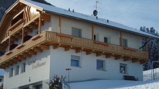 Ein zweistöckiges Gebäude mit Balkon, mit der Aufschrift "Gutshof Erschbaumer", umgeben von schneebedeckten Bäumen.