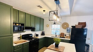 Ett kök med gröna skåp, en svart spis, en vit bänkskiva och en köksö i trä.