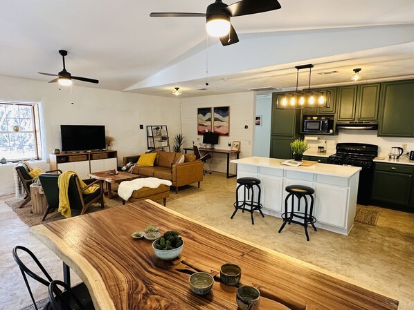 Amplia sala de estar con una mesa de comedor de madera, un sofá y una cocina con armarios verdes y una estufa negra.