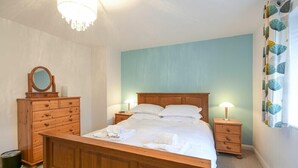 A bedroom with a wooden bed, two bedside tables with lamps, a dresser, and a mirror. - Braidcarr Cottage (Seahouses)