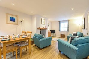 A living room with a wooden dining table, teal sofas, and a fireplace. - Braidcarr Cottage (Seahouses)