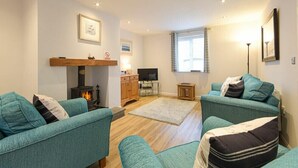 A cozy living room with teal sofas, a fireplace, a TV, and a small table. - Braidcarr Cottage (Seahouses)