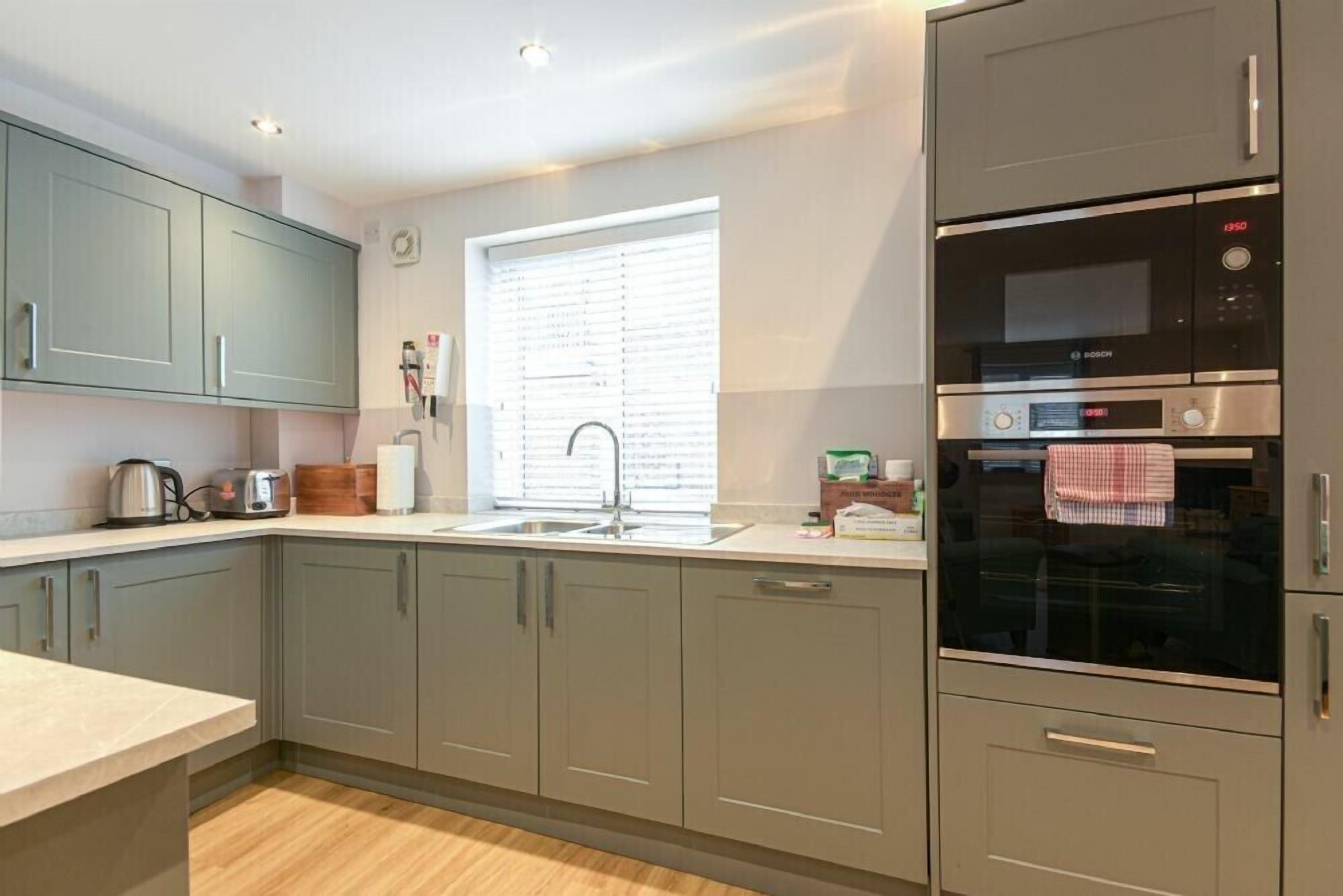 A modern kitchen with grey cabinets, a Bosch oven, and a window with blinds.