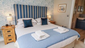 Una cama bien hecha con ropa de cama azul y blanca, dos mesitas de noche con lámparas, una mesita de noche de madera con cajones y un estampado de papel tapiz floral.