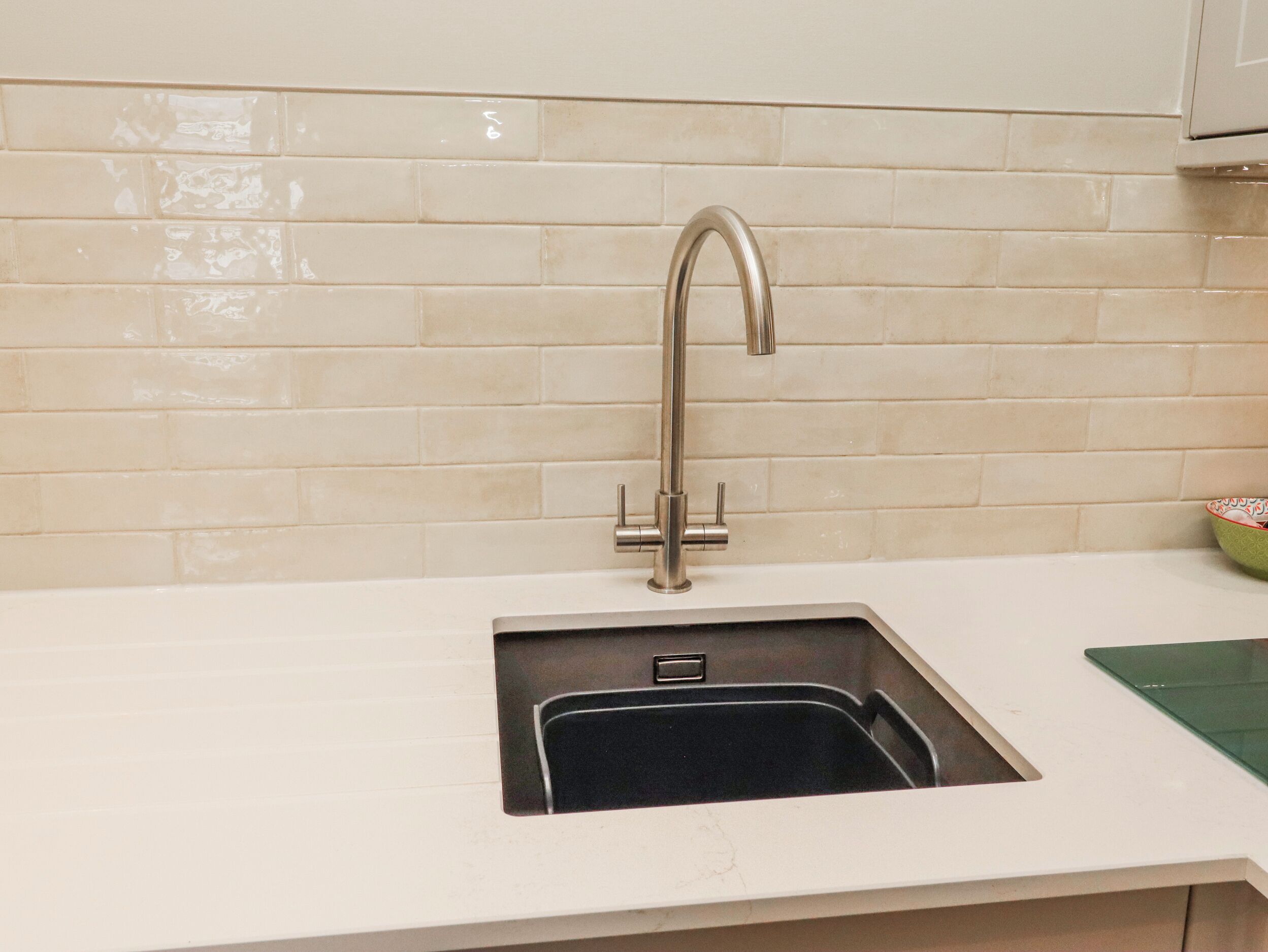 Cozinha com pia de aço inoxidável, torneira e painel de azulejos.