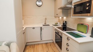 Cocina compacta con armarios blancos, horno de acero inoxidable, microondas y cafetera.