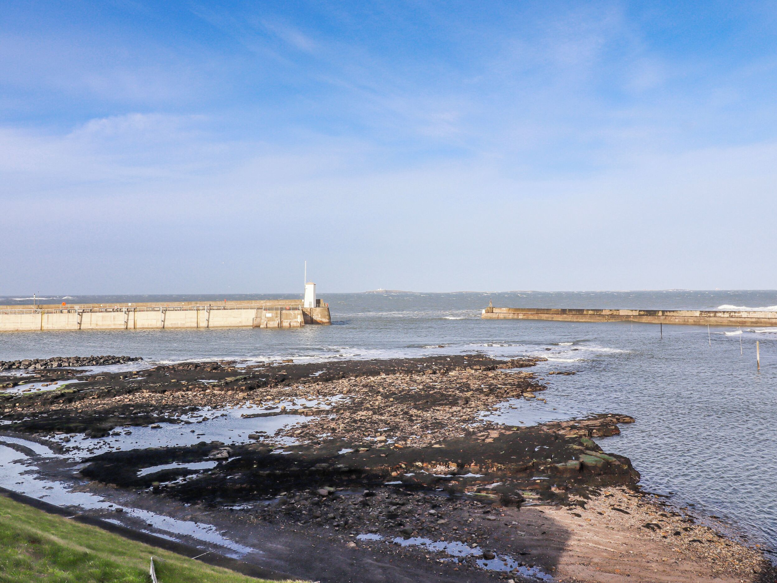 A coastal landscape with a lighthouse, rocky shore, and calm sea.