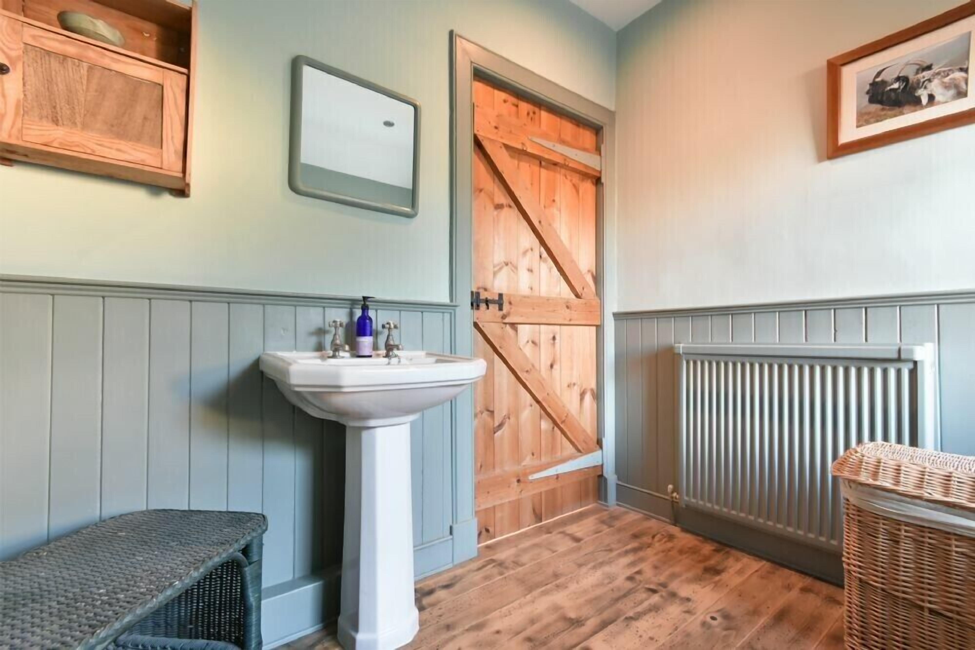 A bathroom with a wooden door, a white sink, a wicker basket, and a framed picture on the wall.