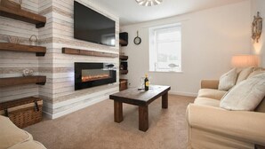 Ein Wohnzimmer mit Kamin, einem flachbildfernseher darüber, einem Holztisch und einem beigefarbenen Sofa.
