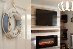 Una habitación con chimenea, un televisor montado encima y un letrero con la palabra 'WELCOME' en la pared.