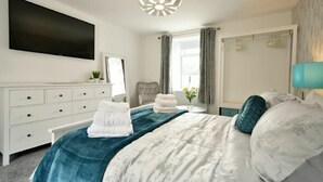 Ein modernes Schlafzimmer mit einem großen Bett, einem Flachbildfernseher, einer Kommode und einem Fenster mit Vorhängen.